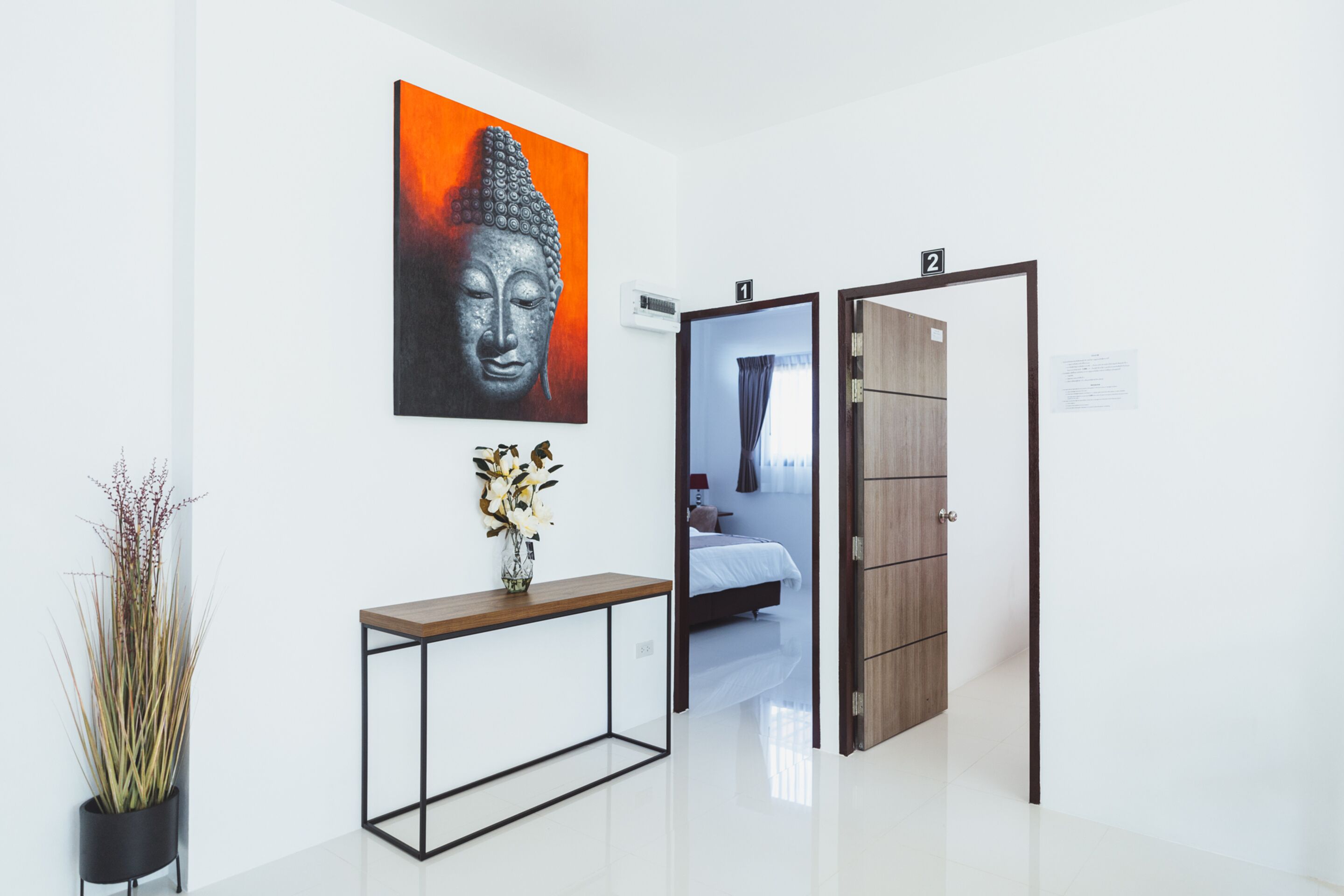 Un hall d’hôtel moderne au design minimaliste, comprenant une console ornée d’un vase de fleurs, un grand tableau représentant un Bouddha et une armoire en bois.