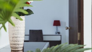 Een kamer met een houten deur, een witte decoratieve vaas met een rode bloem, een rode lamp en een zwarte stoel.