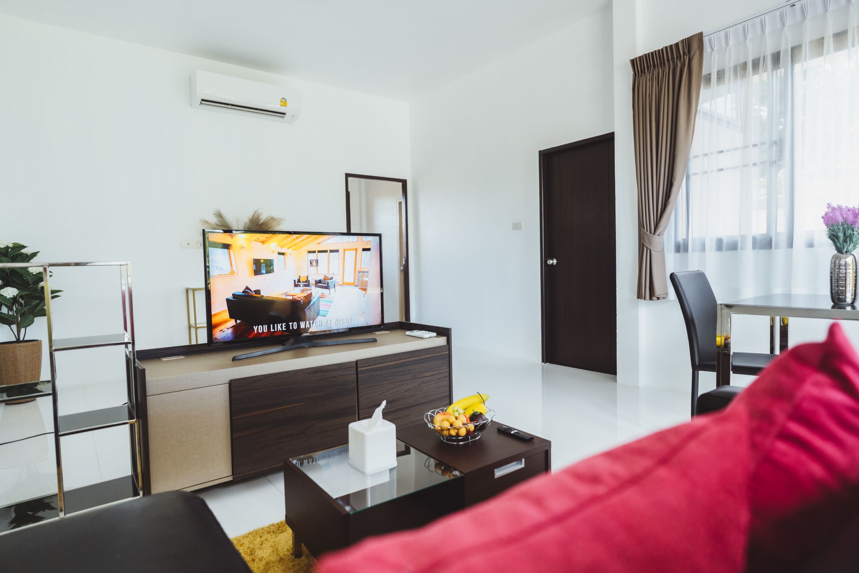 Una sala de estar moderna con una televisión de pantalla plana, una mesa de comedor con sillas y una ventana con cortinas.