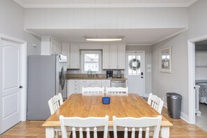 Uma cozinha moderna com armários brancos, uma mesa de jantar de madeira e cadeiras brancas.