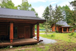 Eine Blockhütte mit Veranda und überdachter Terrasse, umgeben von Bäumen und einer Rasenfläche.