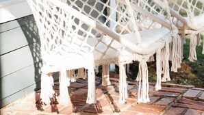 Twee witte macramé hangstoelen aan een veranda.