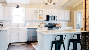 Een moderne keuken met witte kastjes, een centraal eiland met barkrukken, roestvrijstalen apparatuur en een hanglamp.