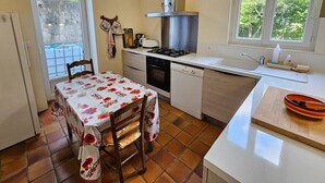 Une cuisine compacte comprenant une table à manger, une cuisinière, un lave-vaisselle et une fenêtre donnant sur un espace verdoyant.
