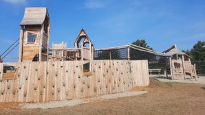 Een houten speelconstructie met klimwanden en een klein huisje.