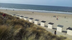 Een strand met mensen die lopen en een rij witte gebouwen met donkere daken.
