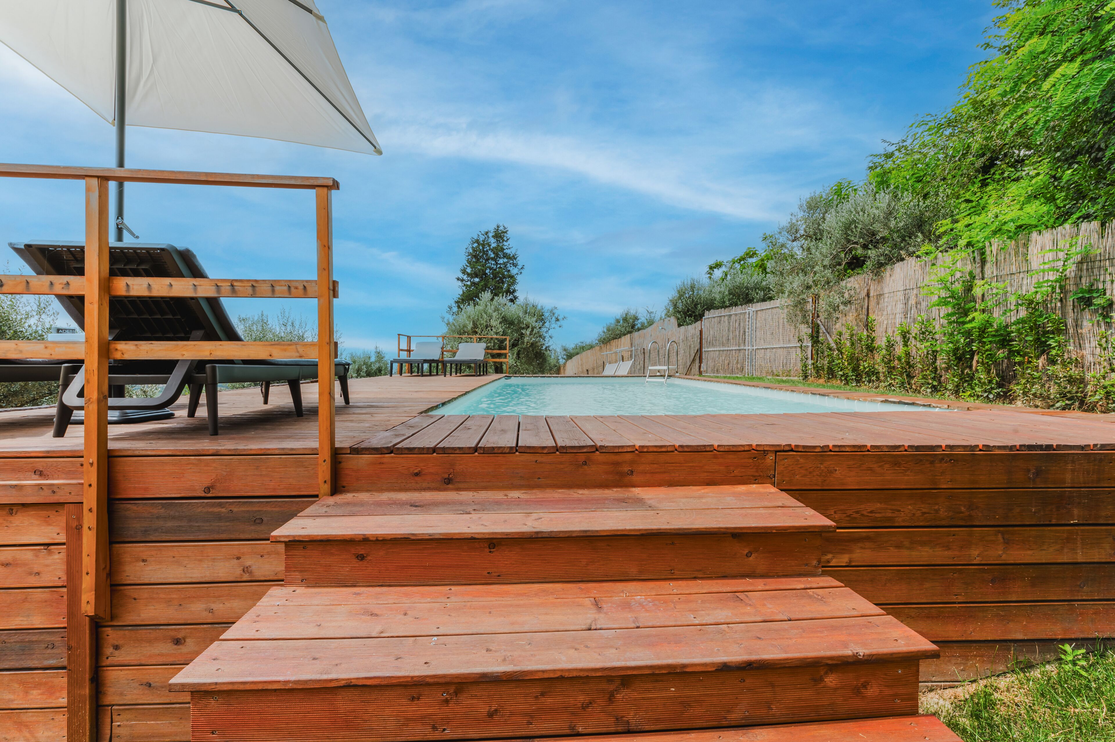 Una terraza de madera con piscina, mobiliario exterior y una valla de madera.