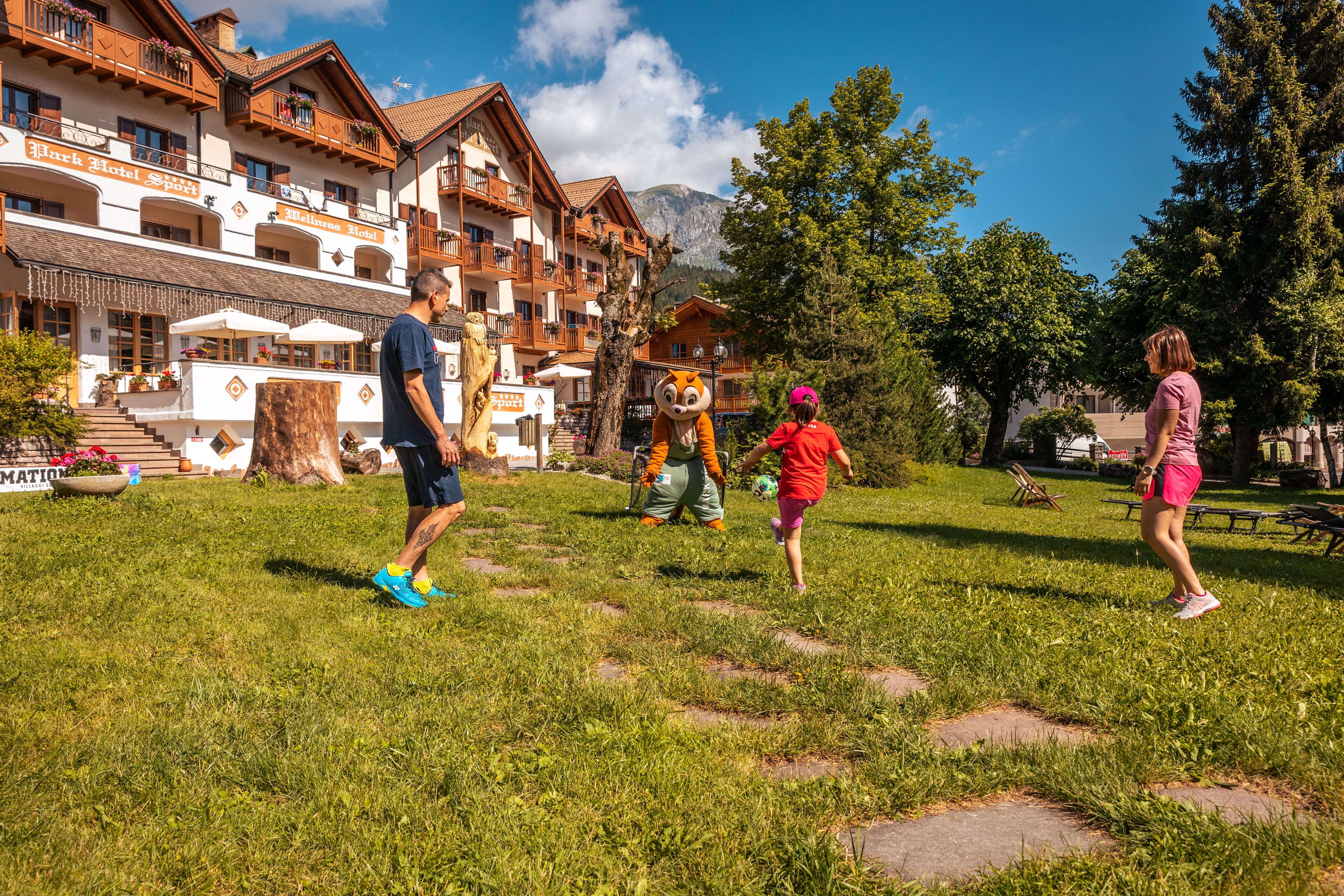 Un hotel con diversi balconi, area salotto all'aperto e montagne sullo sfondo.