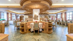 A spacious dining area with wooden furniture and a central column, featuring tables and chairs arranged around it. - Park Hotel Sport (Andalo)