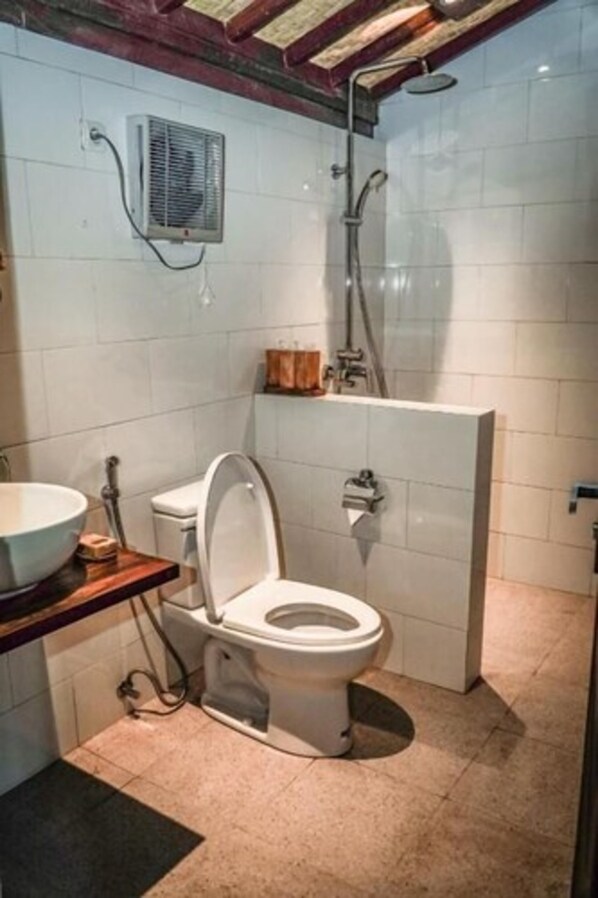 A compact bathroom with a white toilet, a wooden vanity, a shower area, and a wall-mounted air conditioning unit.