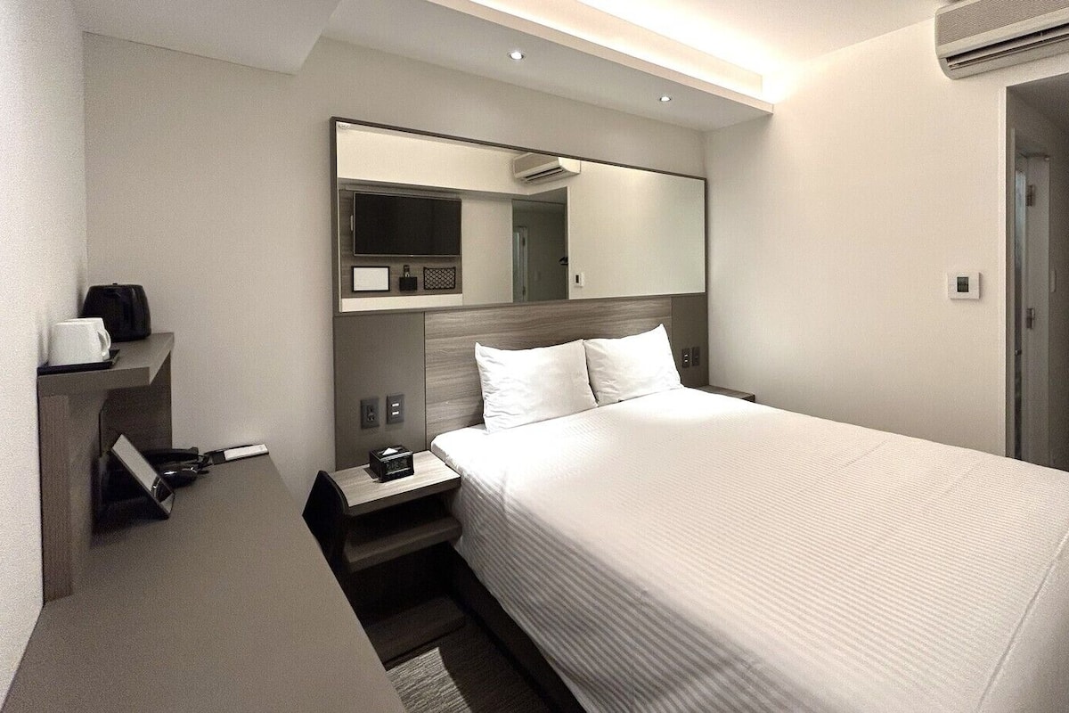 Ein Hotelzimmer mit Bett, Nachttisch, Spiegel, Fernseher und Klimaanlage.