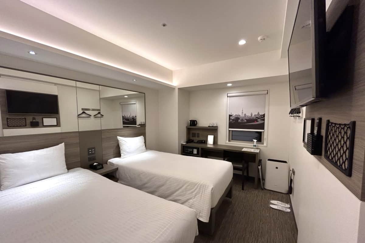 Ein Hotelzimmer mit zwei Betten, einem Schreibtisch, einem Stuhl, einem Fernseher und einer kleinen Mülltonne.