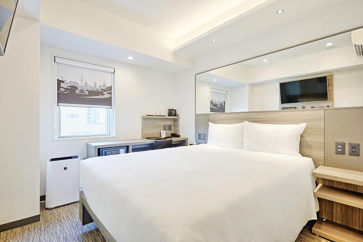 Ein modernes Hotelzimmer mit einem großen Bett, einem Schreibtisch, einem Flachbildfernseher und Blick auf die Stadt.