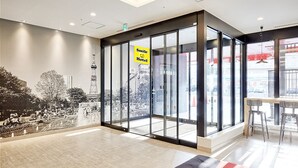 Een hotel lobby met een grote glazen wand, een bordje met Smile Hotel en een uitzicht op een stadsgezicht, inclusief een toren.