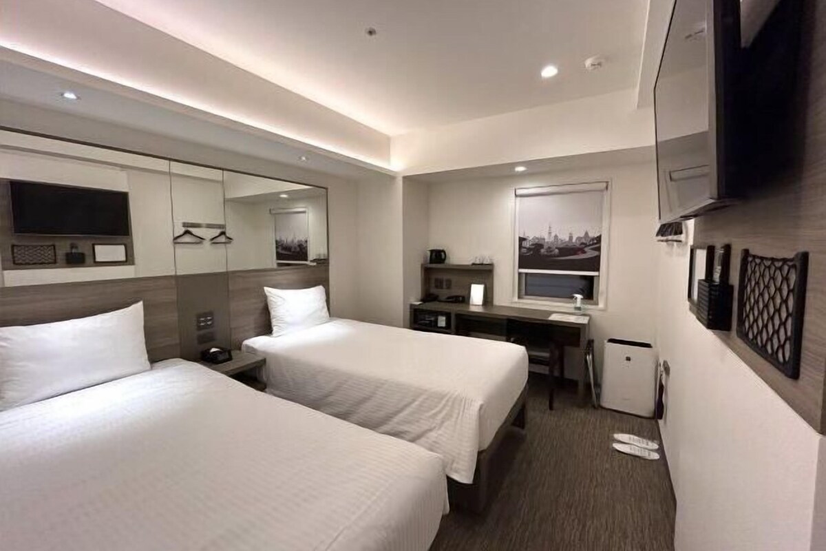 A hotel room with two beds, a desk with a computer, a small fridge, a TV, and a mirror.