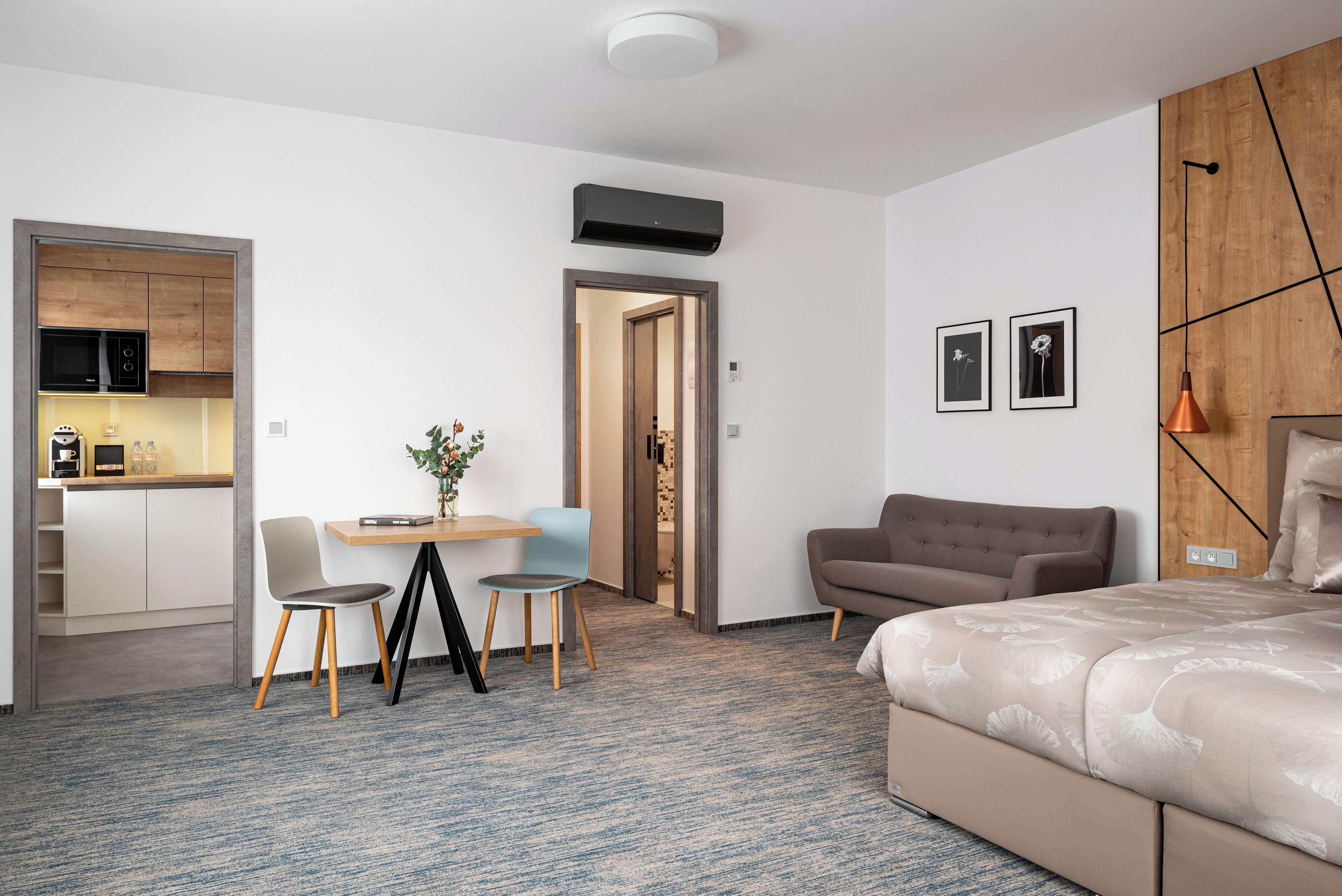 A modern hotel room with a bed, a sofa, a dining area with chairs, and a kitchenette.