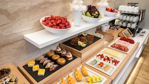 Un buffet proposant une variété de plats, notamment des fruits, des pâtisseries et des fromages.