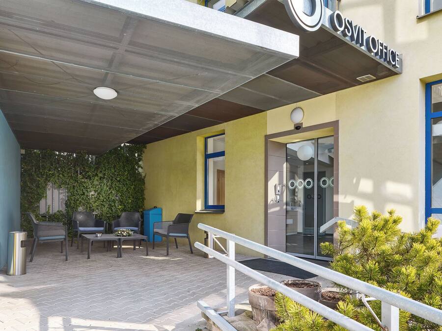 An outdoor seating area with chairs and tables, a covered entrance, and a building with a sign that reads "OSVIT OFFICE".