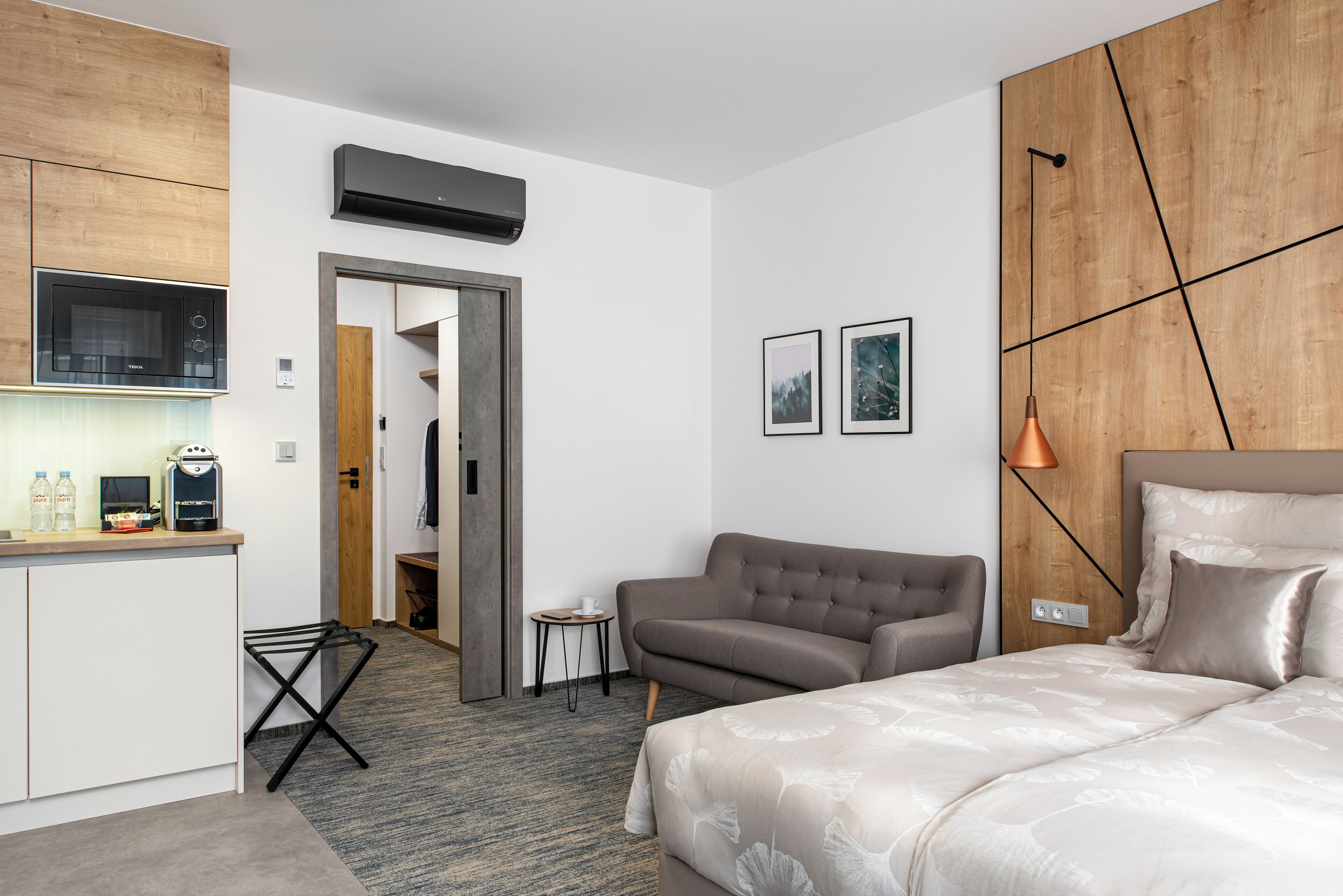 Quarto de hotel moderno com cozinha compacta, cama, sofá e uma pequena mesa lateral.