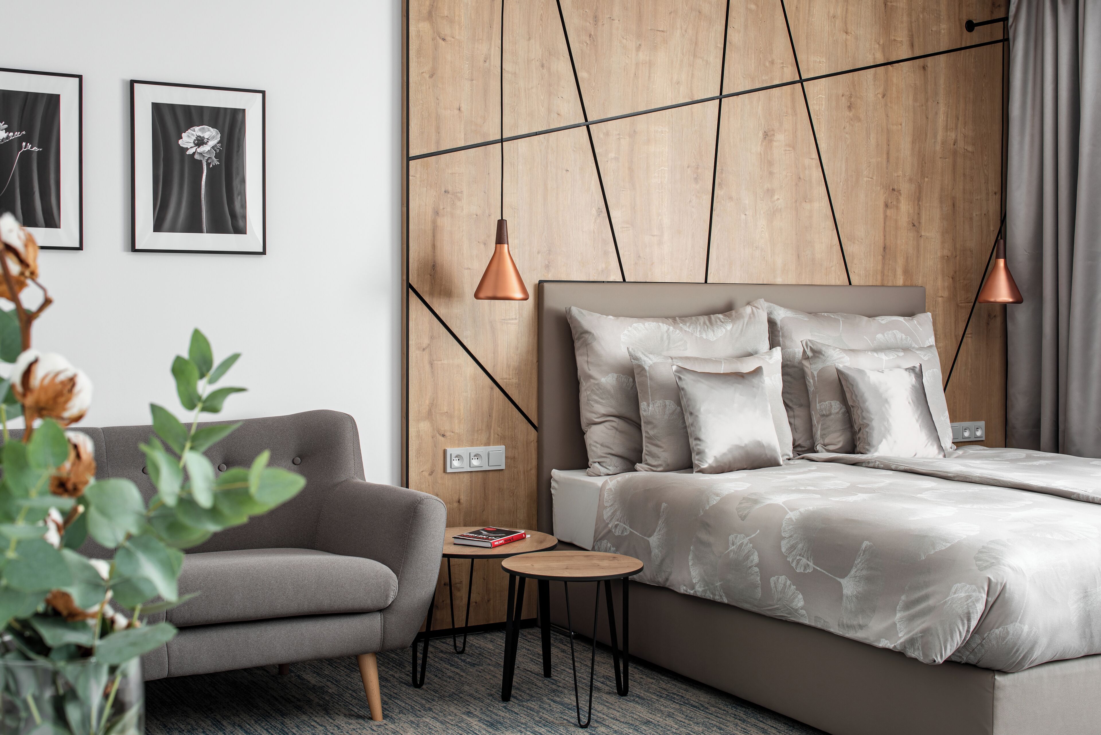 A modern hotel room with a bed, a sofa, a small table, and two wall-mounted picture frames.