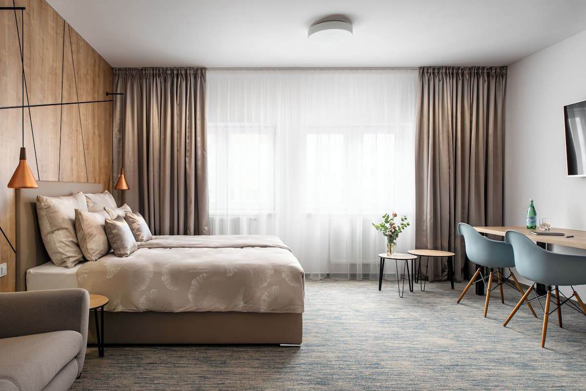 Une chambre d’hôtel moderne, dotée d’un grand lit, d’un bureau avec deux chaises, d’une petite table et d’un téléviseur fixé au mur.