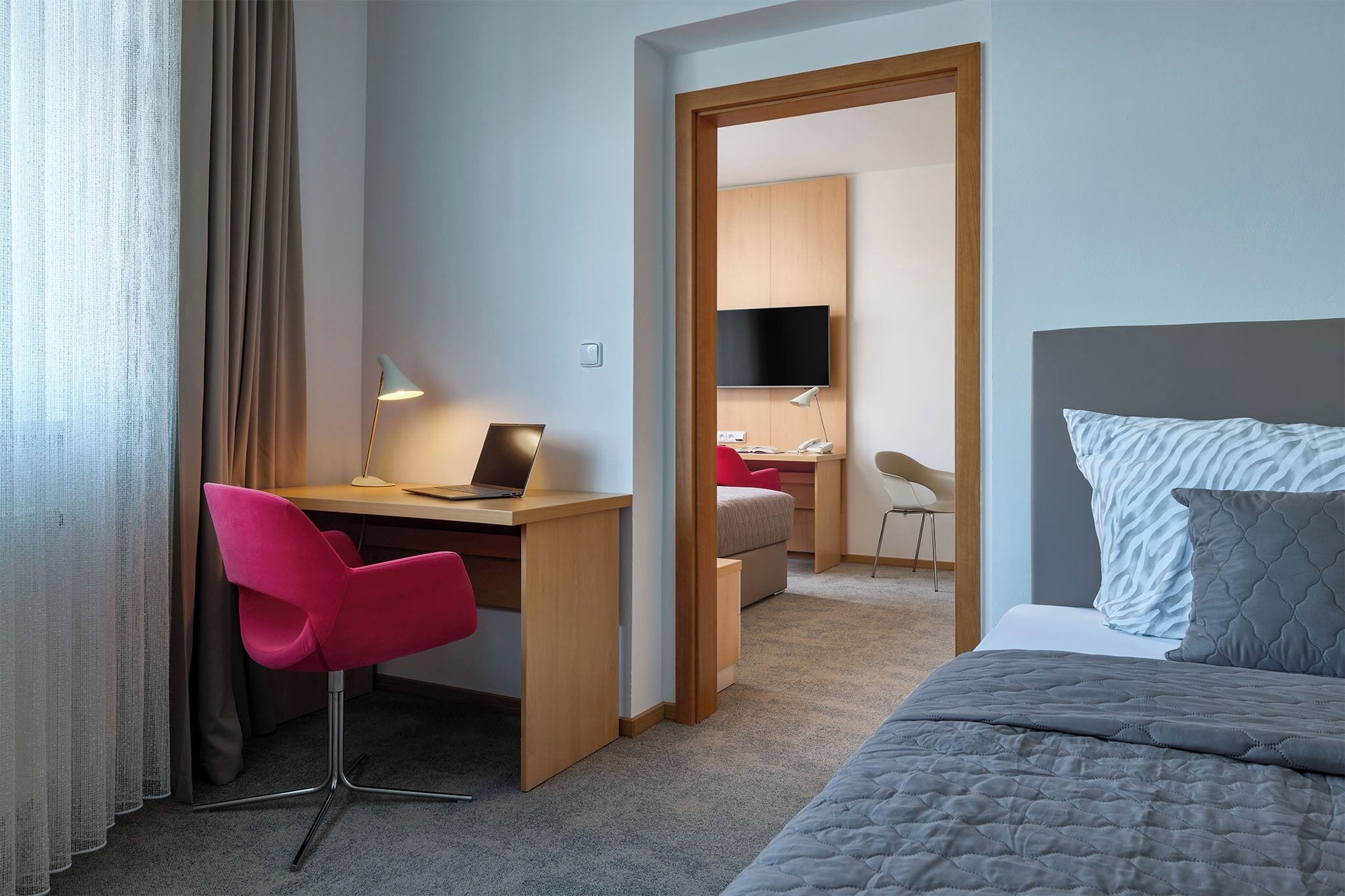 Una habitación de hotel con cama, escritorio, silla, televisor y armario.