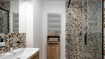 Un baño con lavamanos blanco, mueble de madera y ducha con mosaicos.