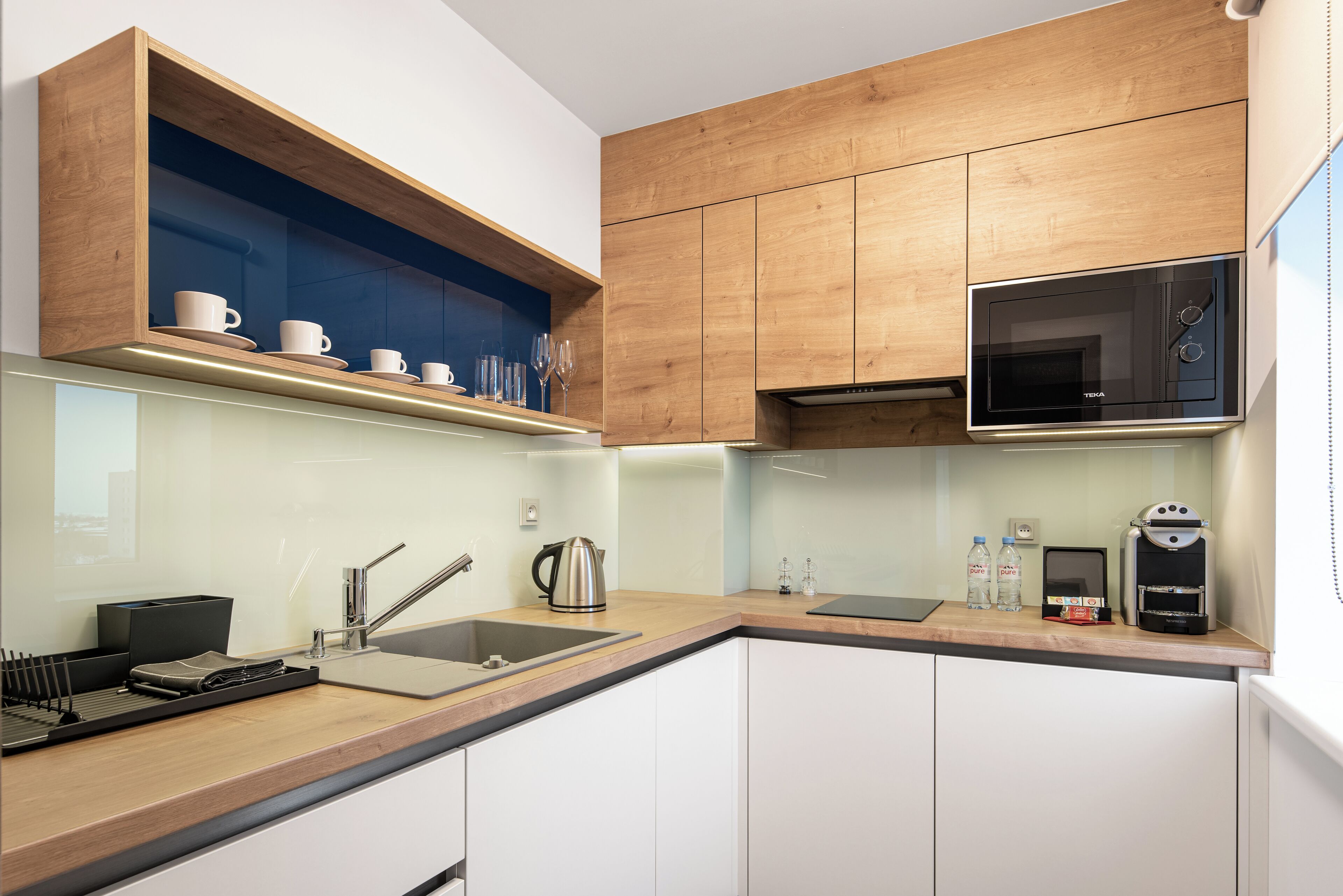 A modern kitchen with wooden cabinets, a built-in microwave, a coffee machine, and a sink.