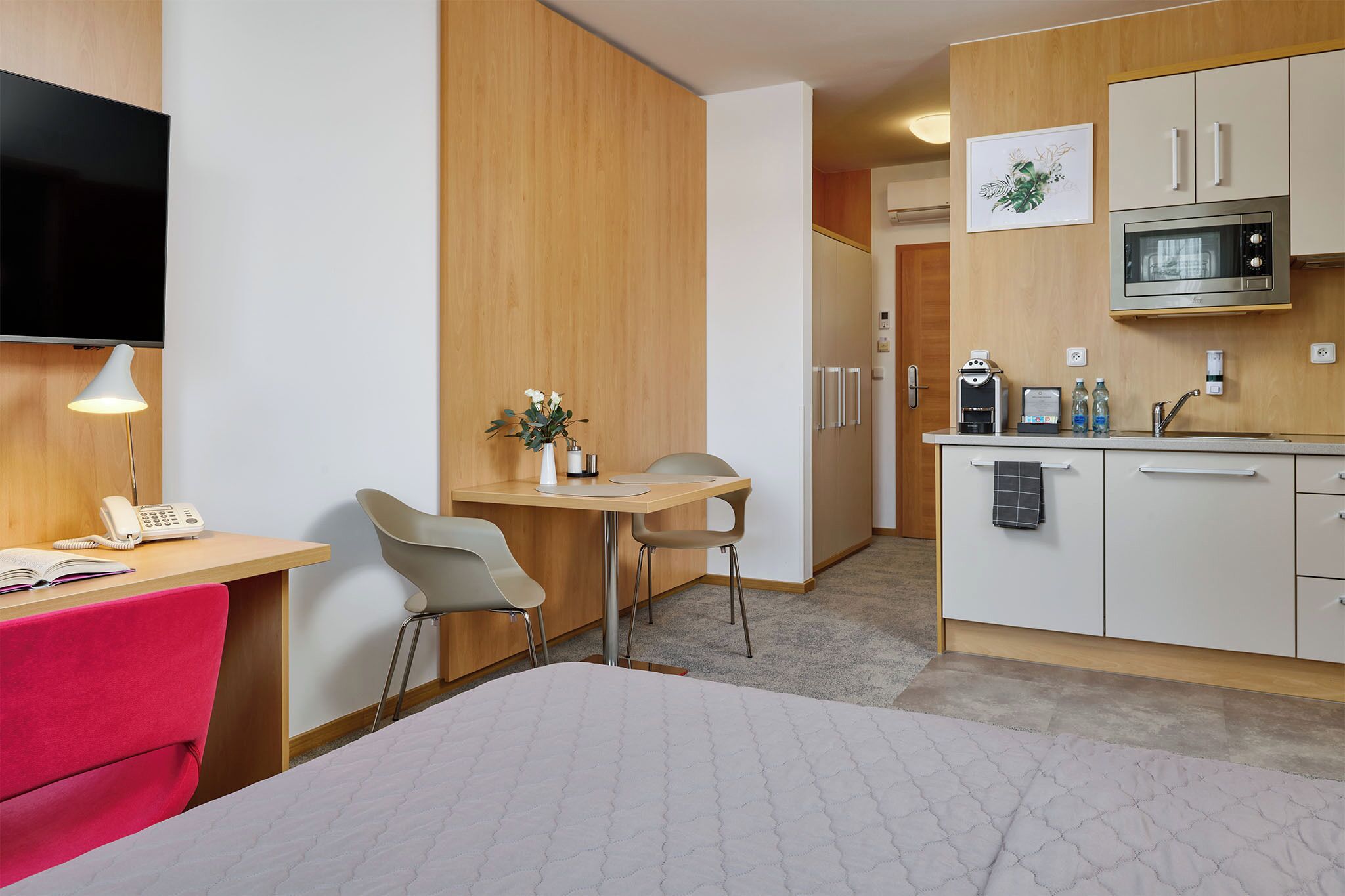 Une chambre d’hôtel comprenant un lit, un bureau avec un téléphone, une chaise, une petite table avec une plante, un four à micro-ondes et un lavabo.