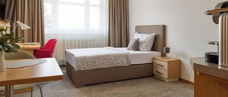 A hotel room with a bed, a desk, a chair, a TV, and a bedside table.
