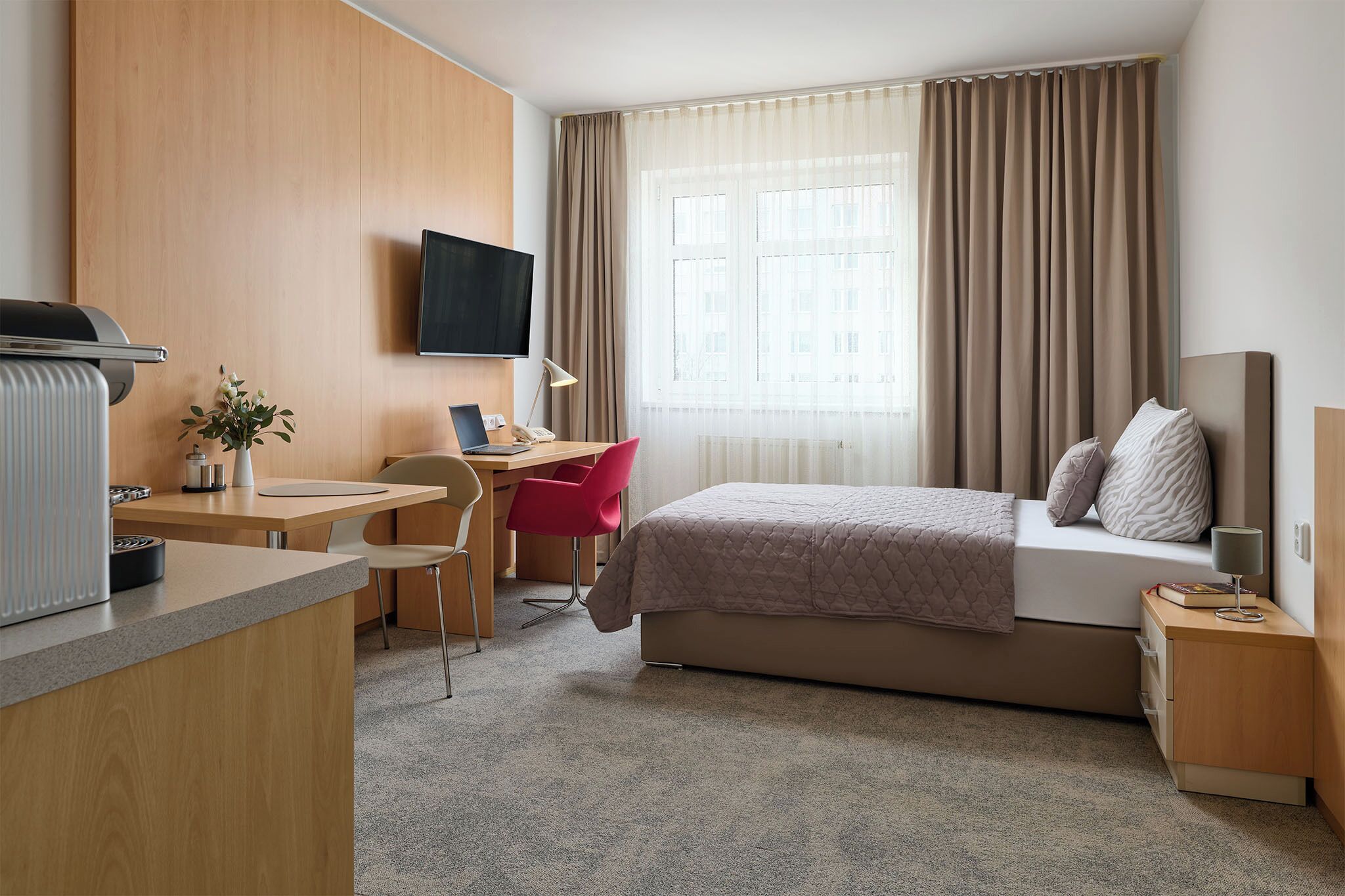 A hotel room with a bed, desk, chair, TV, and curtains.