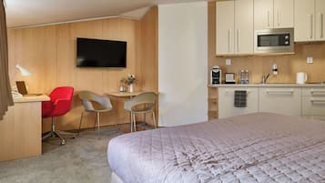 A hotel room with a bed, a desk with two chairs, a television, a microwave, and a small kitchenette.