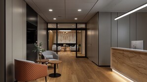 Un espace d’accueil moderne avec un comptoir de réception en bois, un coin salon avec une table ronde et des chaises, et une vue sur une salle à manger agrémentée d’un lustre.