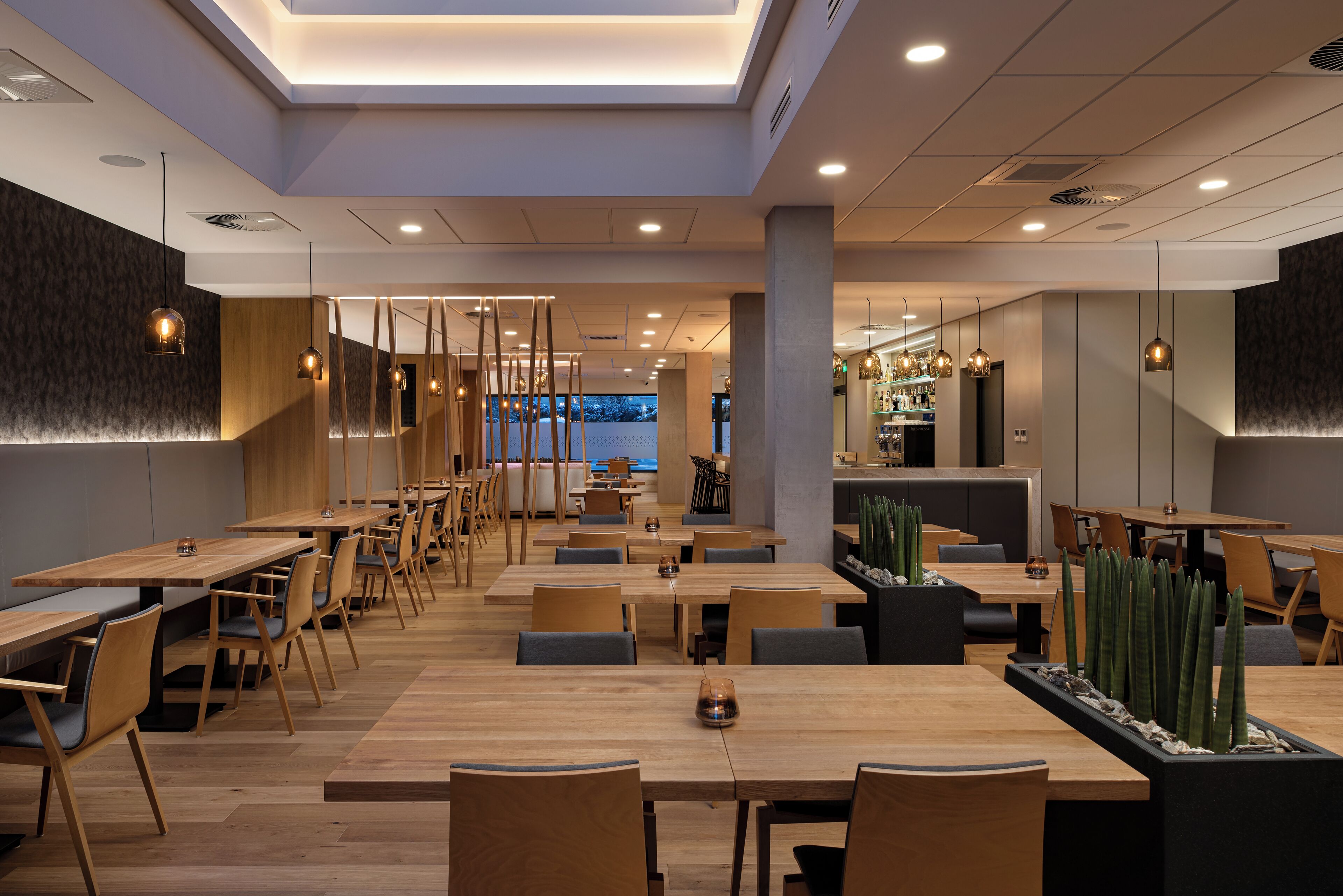 Een modern restaurant met houten tafels en stoelen, hanglampen en uitzicht op de stad.