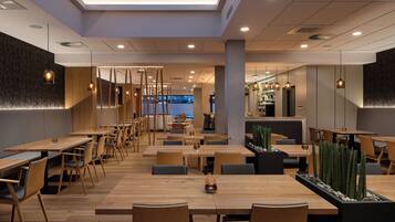 Een modern restaurant met houten tafels en stoelen, hanglampen en uitzicht op de stad.