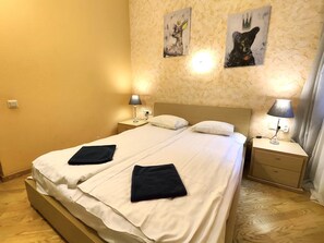 Une chambre d’hôtel avec un lit double, deux tables de chevet avec des lampes, une tête de lit et deux œuvres d’art accrochées au mur.