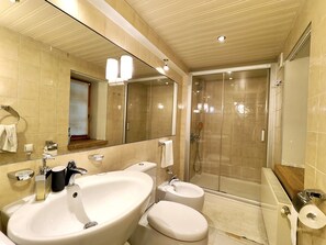 Une salle de bain dotée d’un grand lavabo, de deux toilettes, d’une douche en verre et d’un miroir avec éclairage intégré.