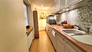 Een smalle keuken met een betegelde spatwand, een spoelbak en een kookplaat.