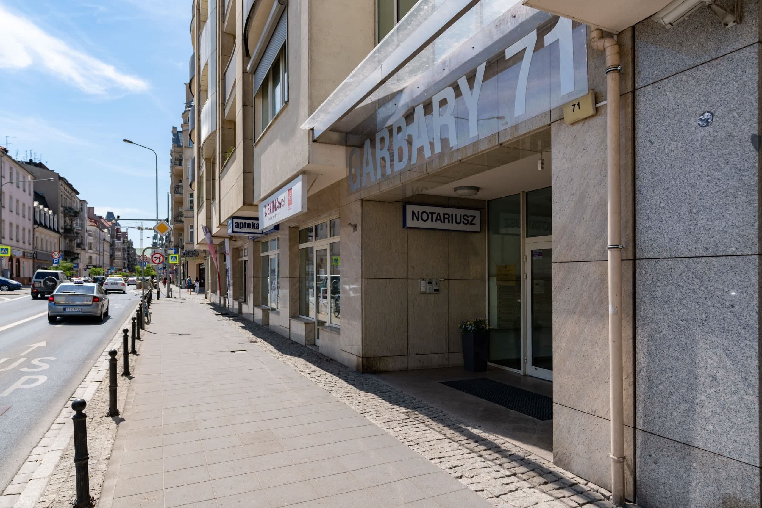 Una vista di strada con un edificio con la scritta 'CARBARY 71' e 'NOTARIUSZ'.