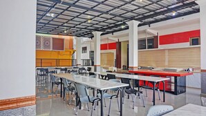 A modern dining area with multiple tables and chairs, a kitchen area with red accents, and a ceiling with exposed beams.