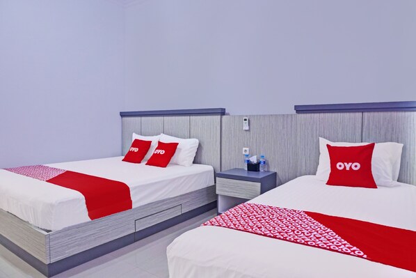 Una habitación de hotel con dos camas, cada una con una colcha roja y blanca, y almohadas a juego. Hay una mesita de noche entre las camas con una botella de agua y un teléfono.