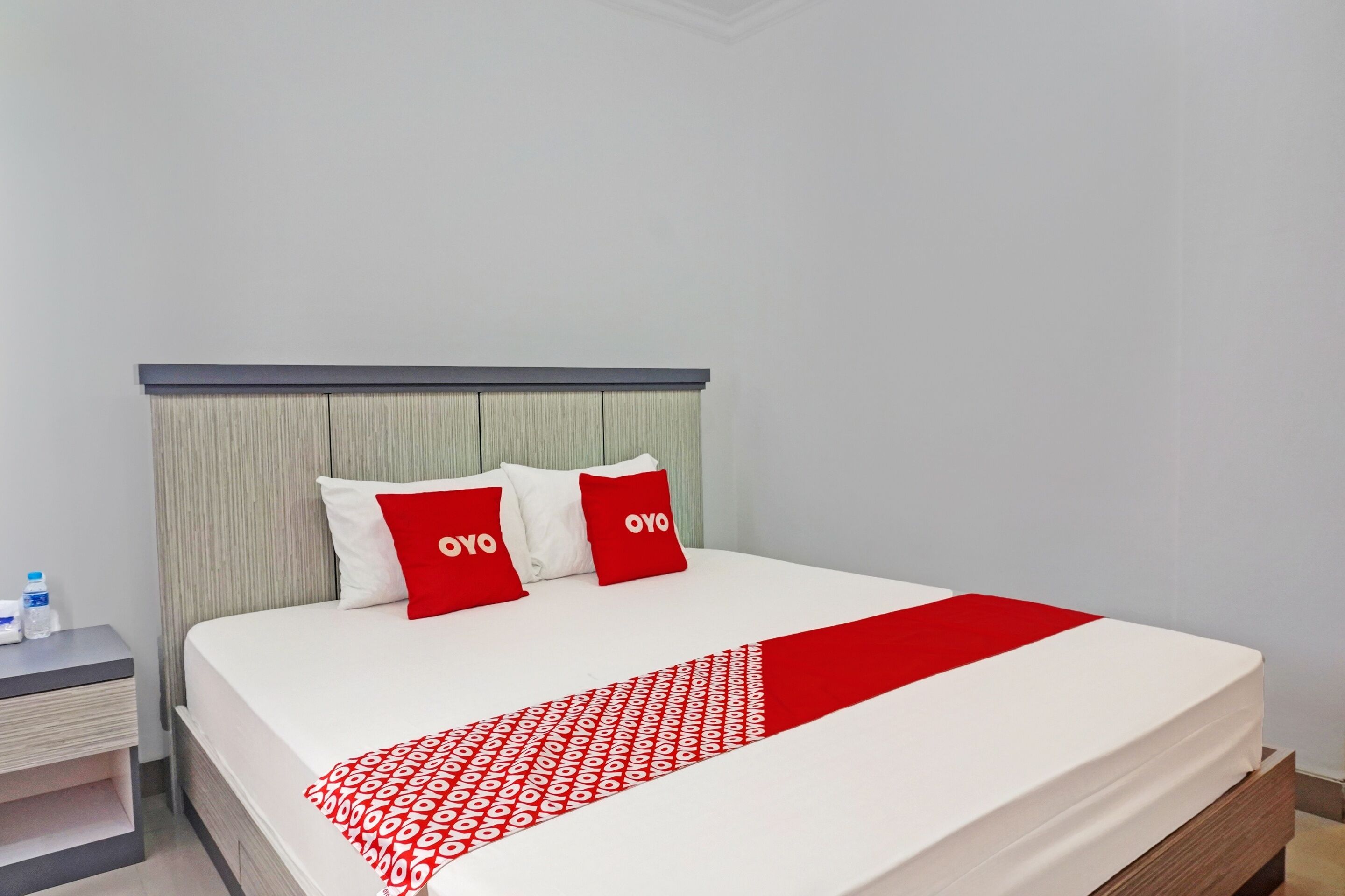 A neatly made bed with a white and red bedspread, two red pillows with the word "OYO" on them, and a grey headboard.