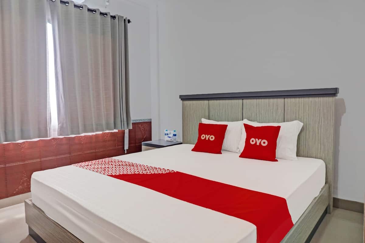 A hotel room with a large bed, two red pillows with the word "OYO" on them, a white bedspread, and a red blanket.