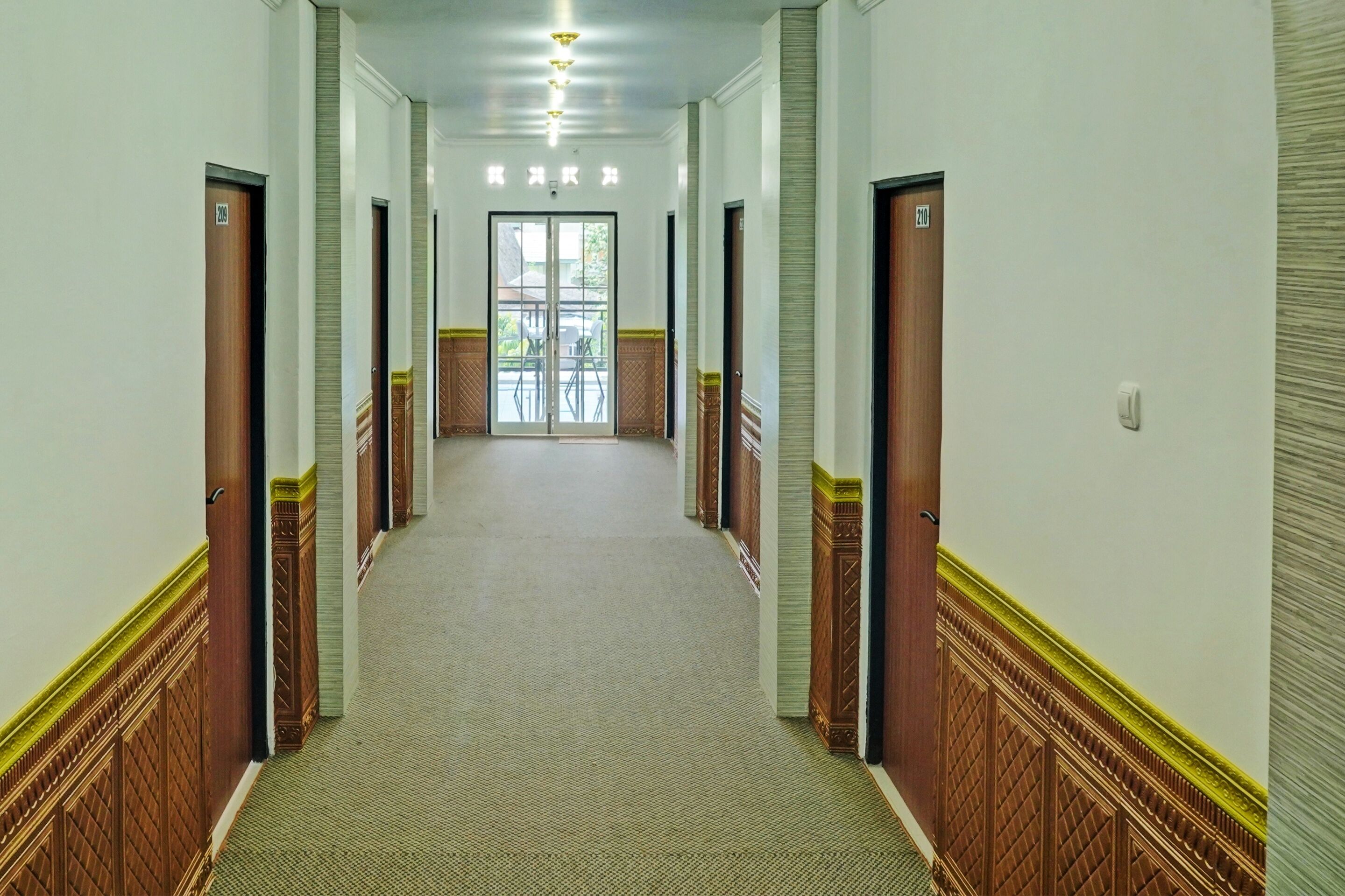 A long, narrow hallway with wooden doors on both sides, leading to a glass door at the end.