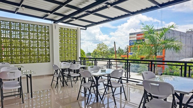 A spacious outdoor seating area with multiple tables and chairs, a decorative lattice wall, and a view of a building with signage.