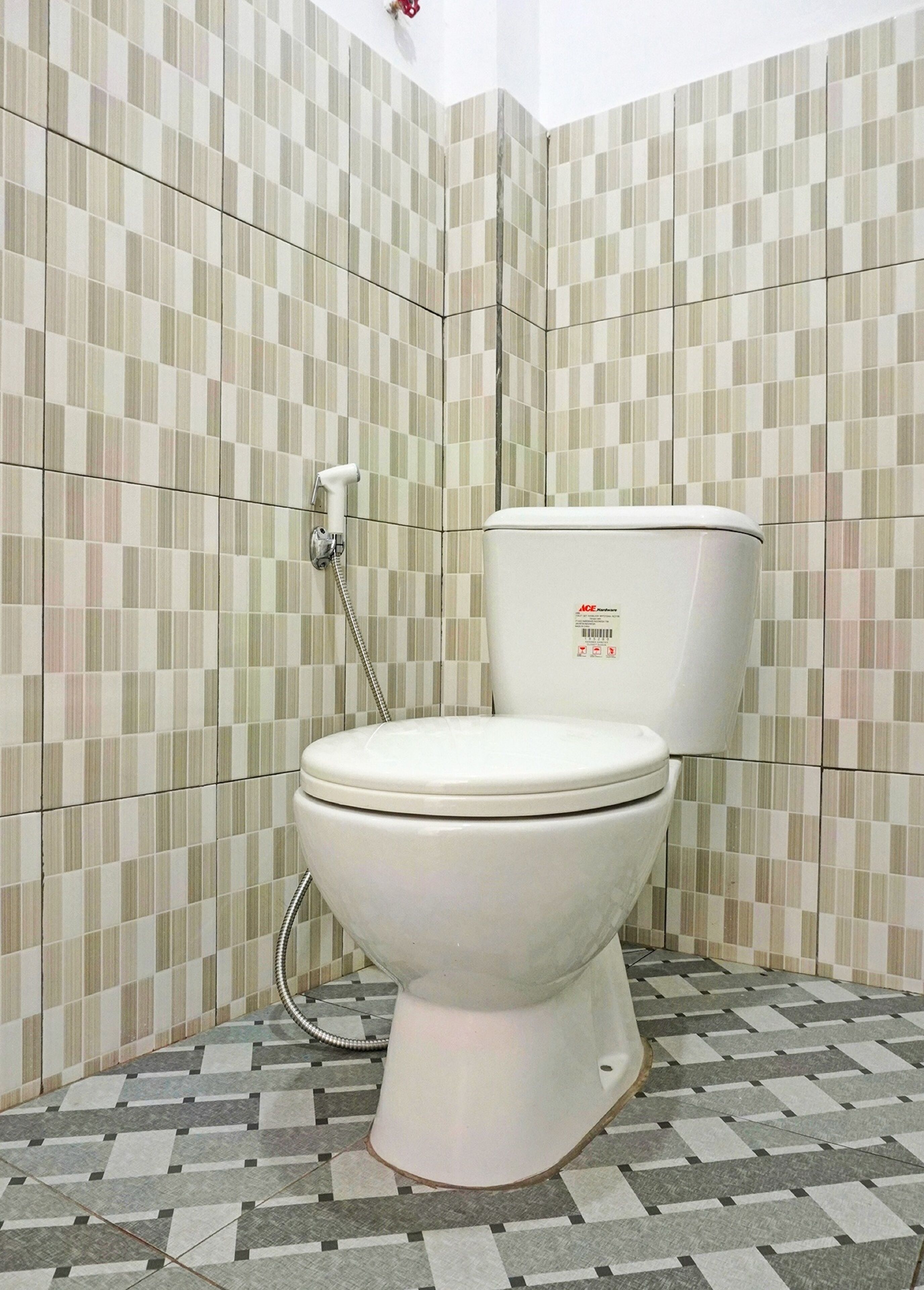 A toilet with a hinged lid, a wall-mounted flush handle, and a toilet paper holder.