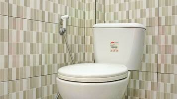 A toilet with a hinged lid, a wall-mounted flush handle, and a toilet paper holder.