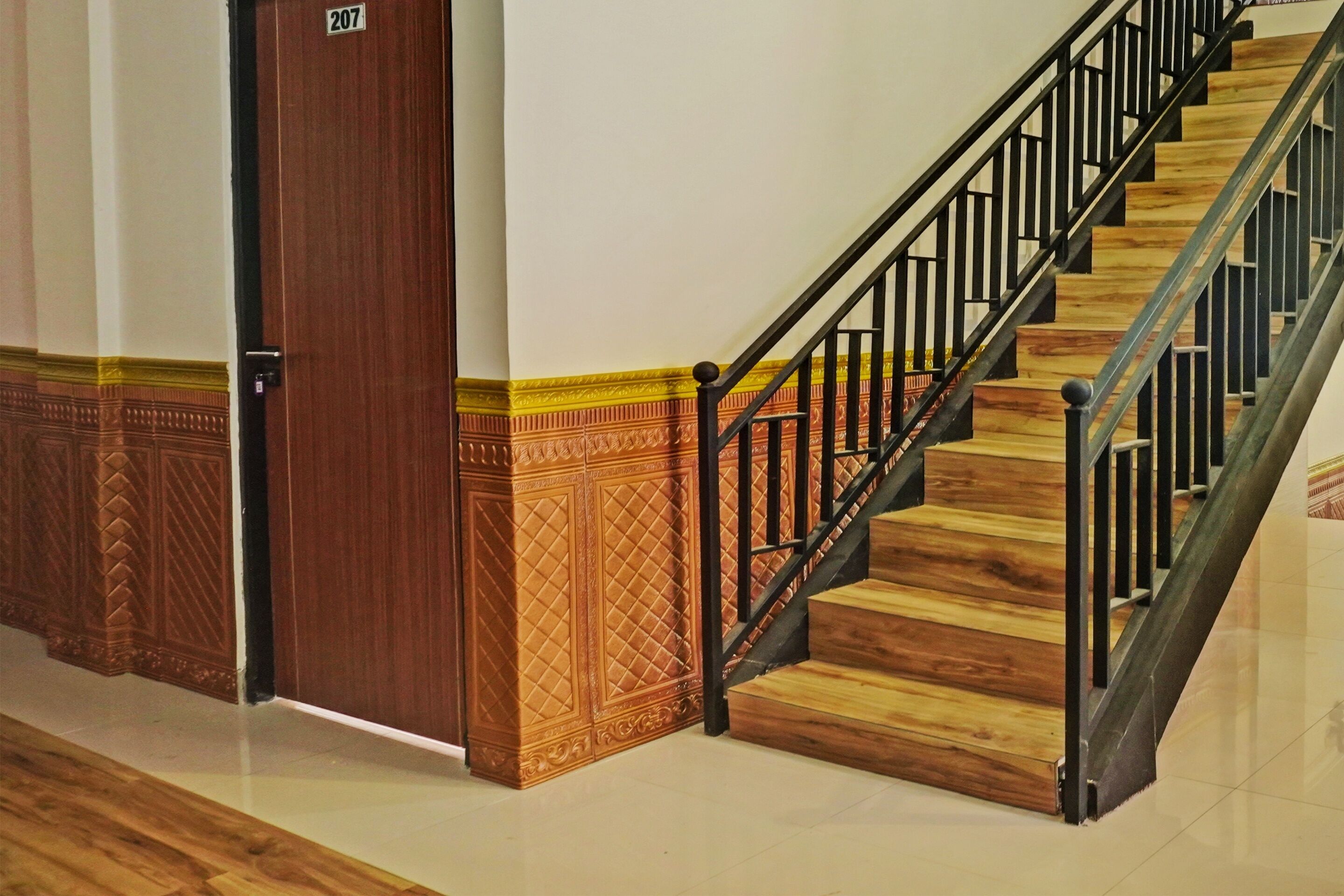 A wooden staircase with black railings and a door labeled "207" in a hallway with patterned flooring.