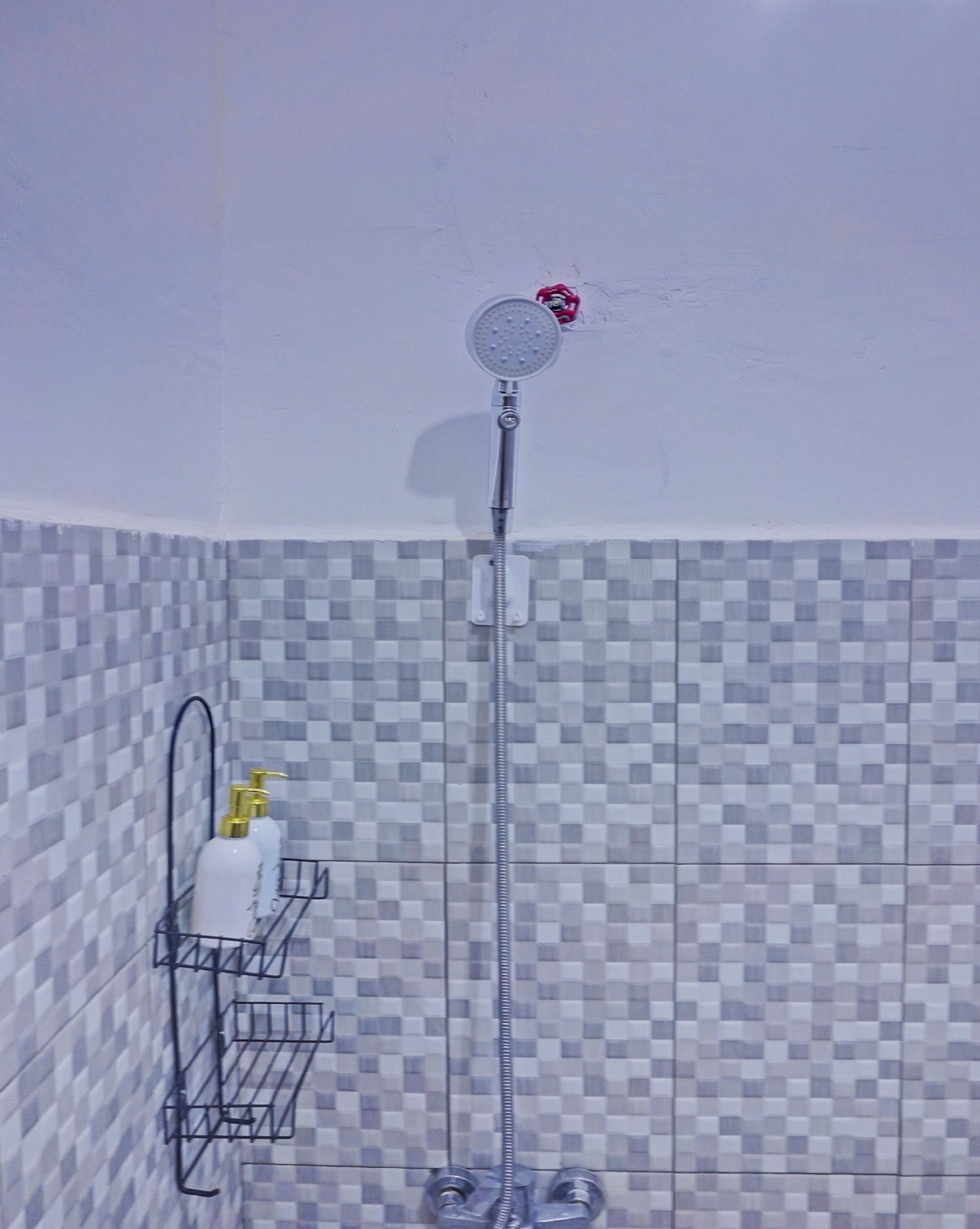 Ducha con cabezal de ducha de mano, grifo empotrado en la pared y pared cubierta de azulejos con diseño a cuadros.
