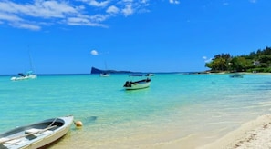 Une plage bordée d’une eau turquoise et limpide, avec des bateaux et une île qui se dessine à l’horizon.